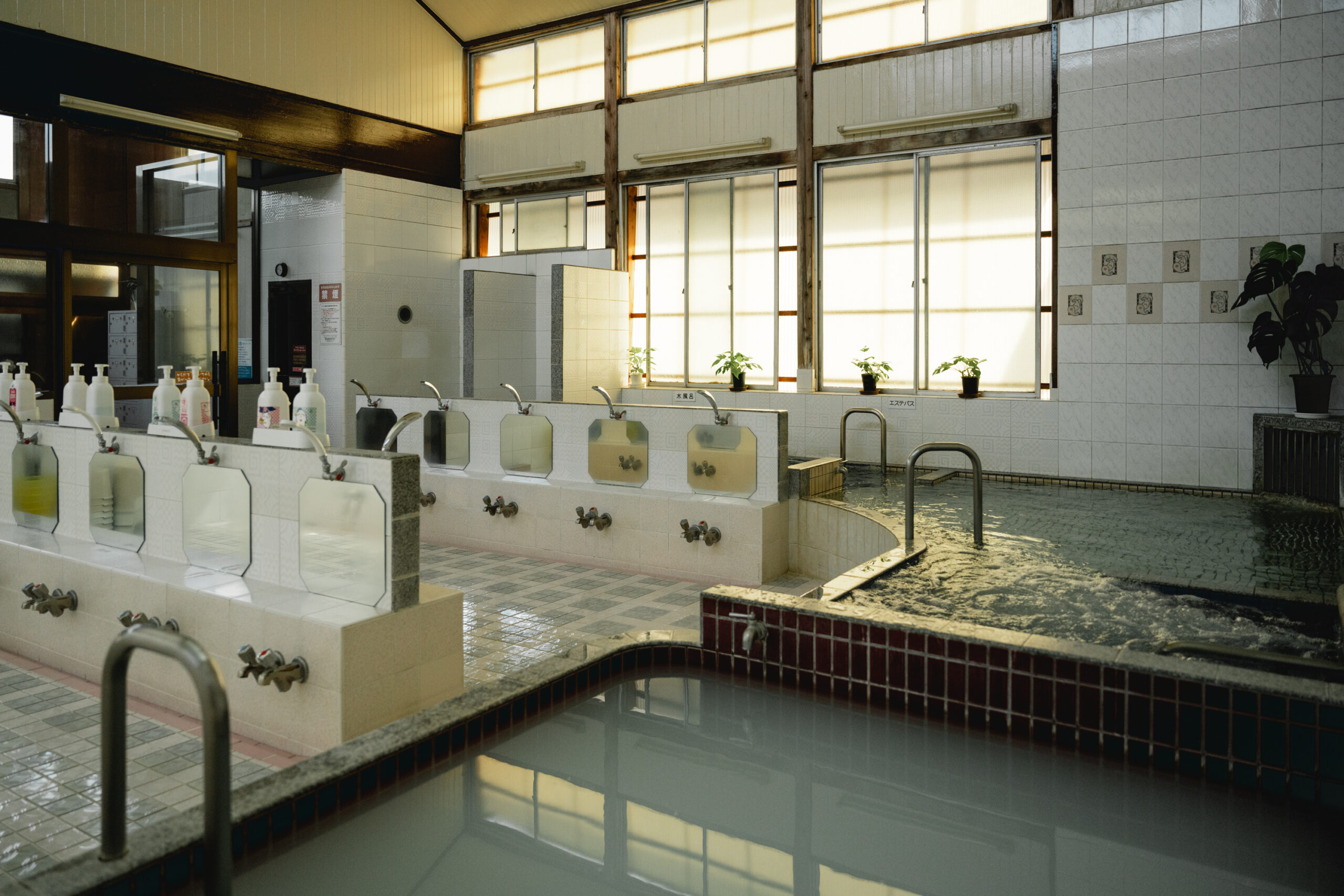 清潔感のあふれる洗い場に夕日が差し込む。　<a href="https://sento-to-machi.org/kita-ku/2024/03/31/tsurunoyu/">▶︎鶴の湯とまちについて</a>